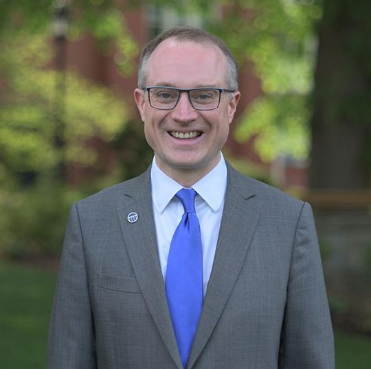 headshot of man in suit and tie, wearing glasses